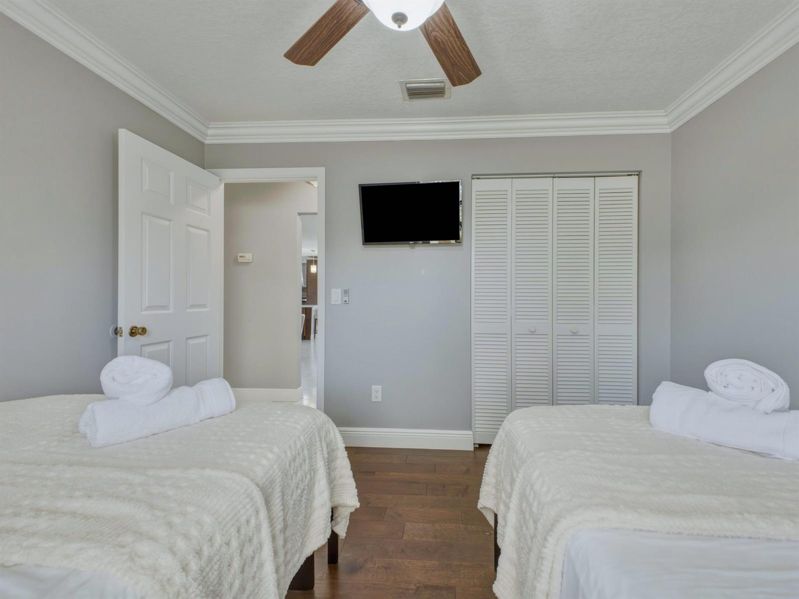 A bedroom with two beds, a wall-mounted television, and white louvered closet doors — 1127 Sea Pines Way, Lantana FL 33462, LANTANA, FL