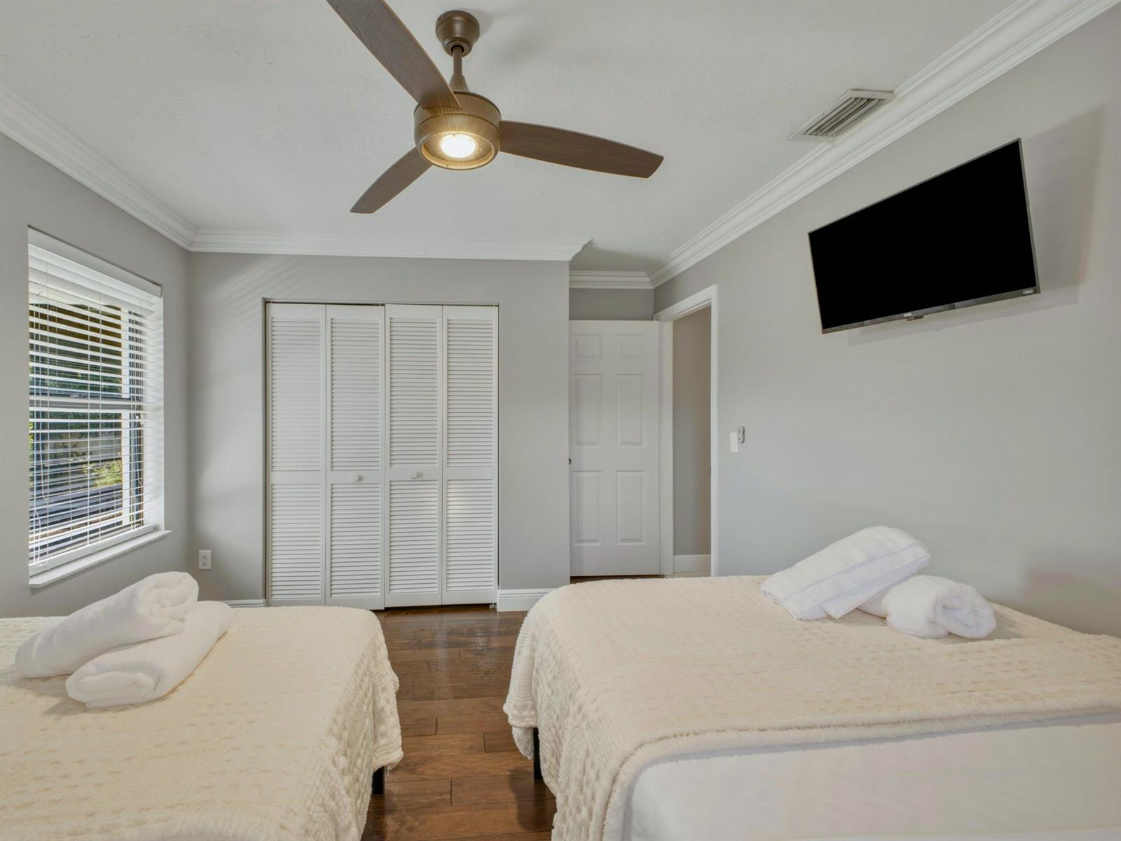 A bedroom features two beds, a ceiling fan, a wall-mounted television, and white louvered closets — 1127 Sea Pines Way, Lantana FL 33462, LANTANA, FL