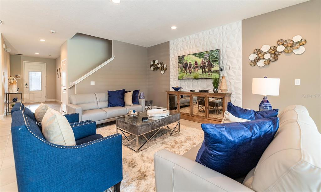 A living room features a textured accent wall, a television, and blue and grey furniture — 7454 MARKER AVENUE, KISSIMMEE, FL