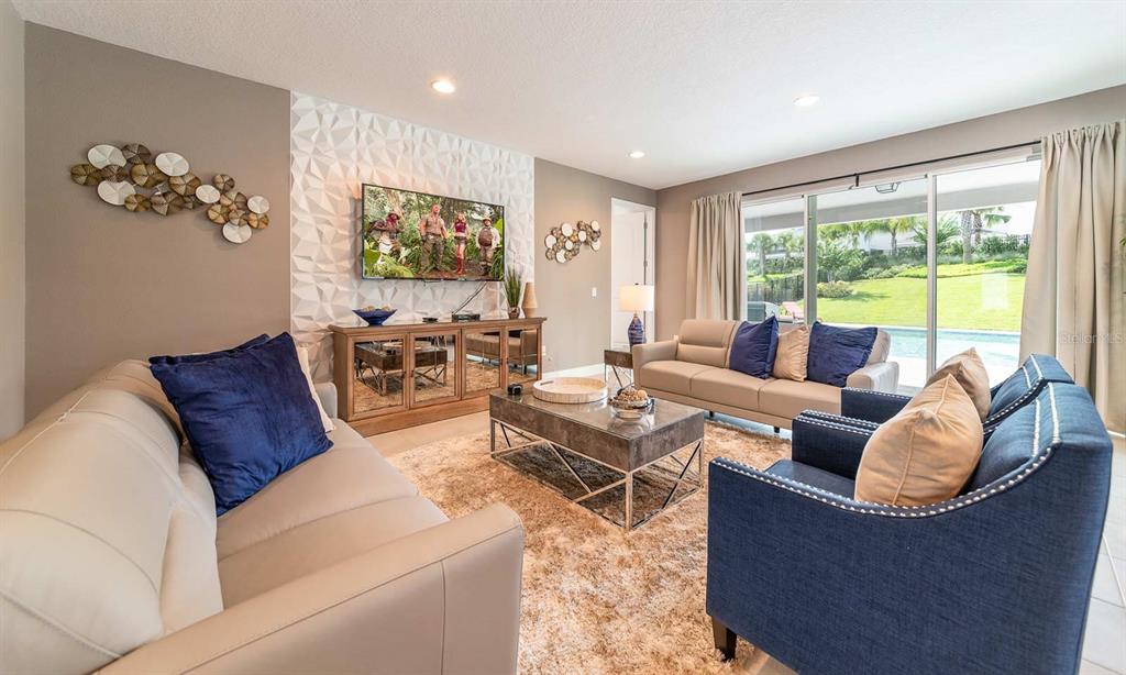 A living room features a textured accent wall, a television, and views of a pool — 7454 MARKER AVENUE, KISSIMMEE, FL