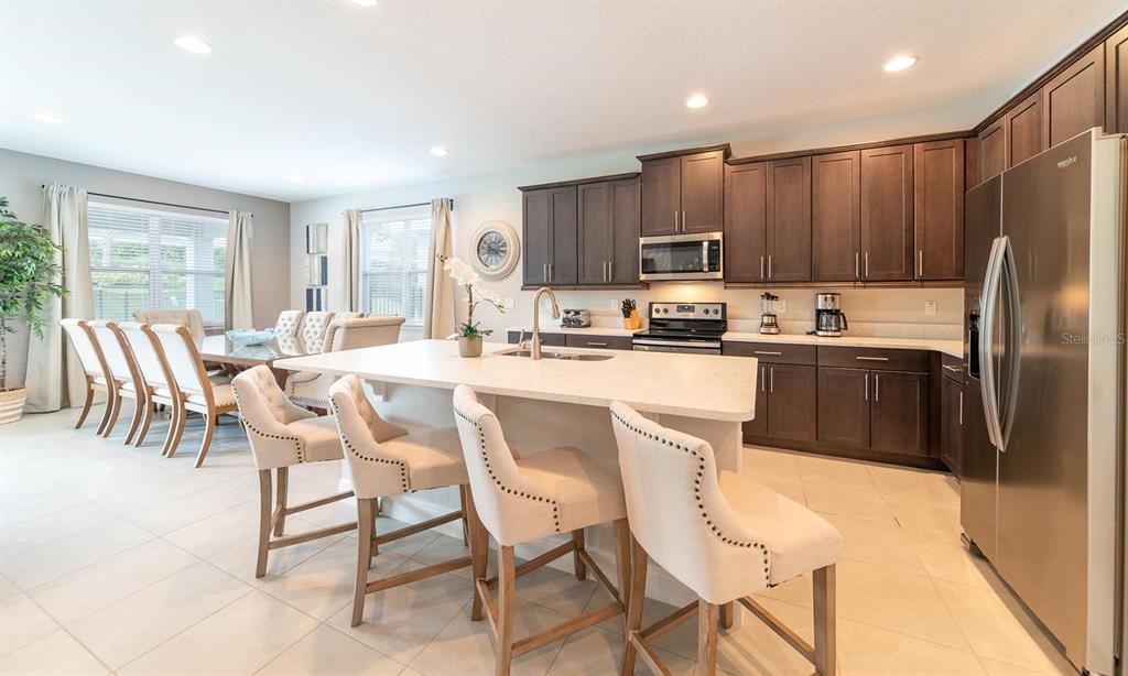 A kitchen with dark wood cabinets, a large white island, and bar stools — 7454 MARKER AVENUE, KISSIMMEE, FL