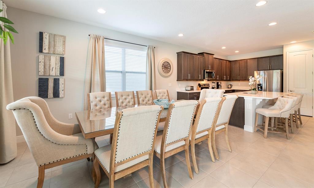 A dining area with a glass table and upholstered chairs sits adjacent to a kitchen — 7454 MARKER AVENUE, KISSIMMEE, FL