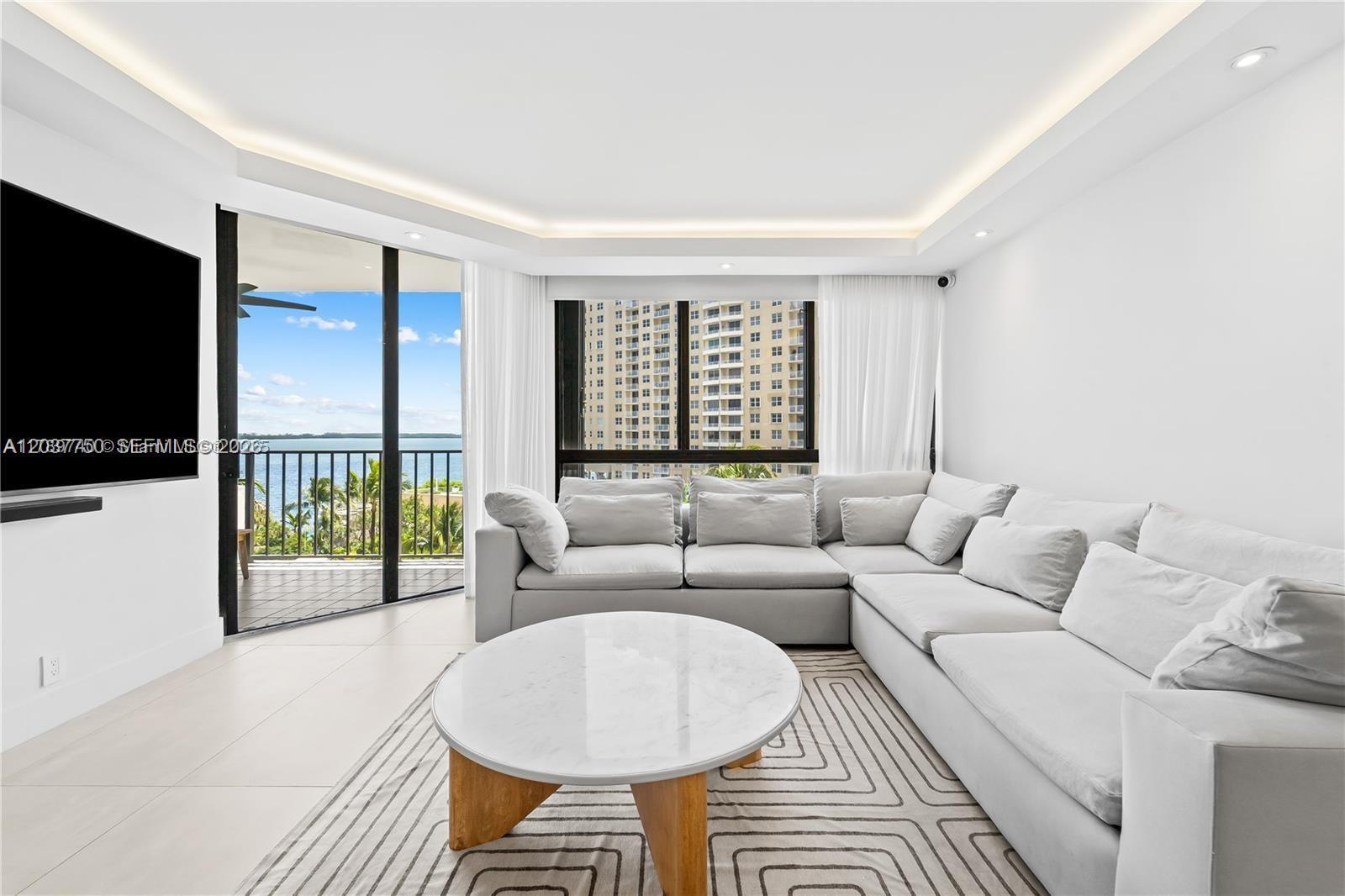 A modern living room features a large sectional sofa, marble coffee table, and balcony view — 520 Brickell Key Dr # A713, Miami FL 33131, MIAMI, FL