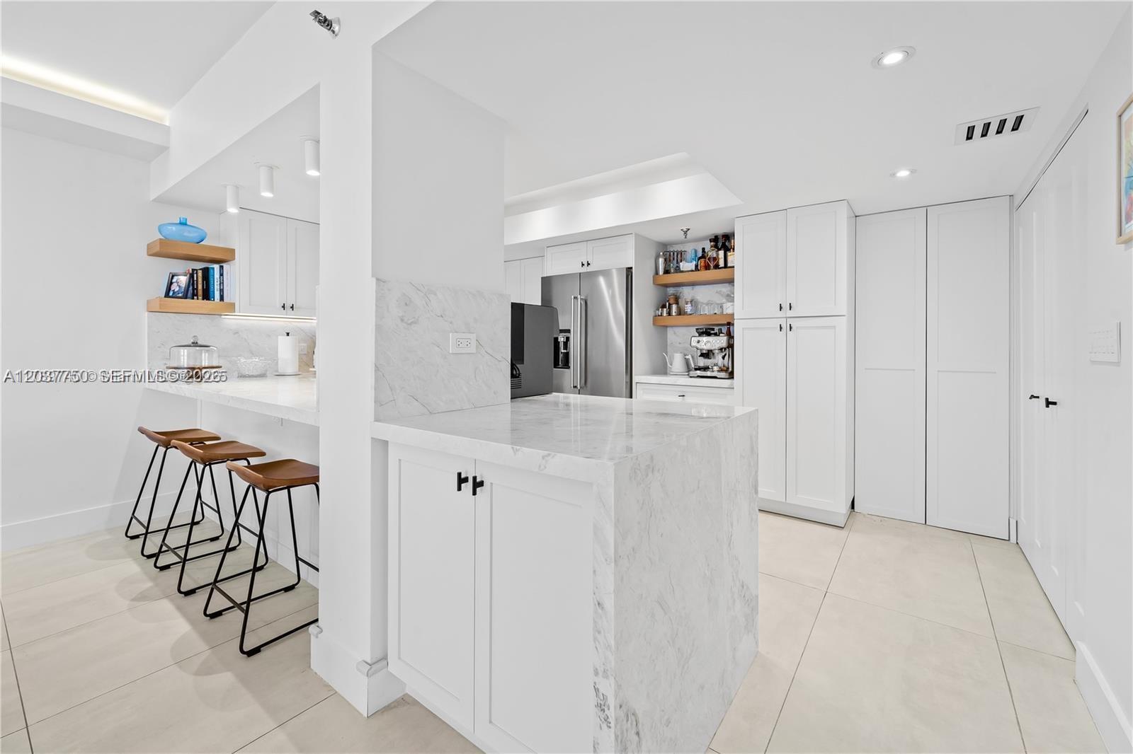 A modern kitchen features white cabinetry, marble countertops, and a breakfast bar with stools — 520 Brickell Key Dr # A713, Miami FL 33131, MIAMI, FL
