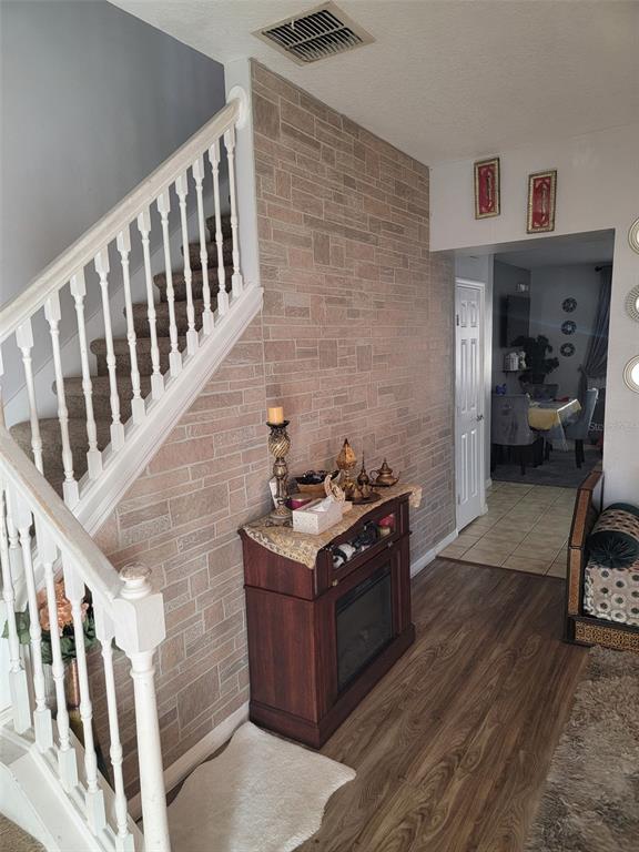 A staircase with white railings stands beside a stone-accented wall and a small electric fireplace — 2682 MAYAGUANA STREET, KISSIMMEE, FL