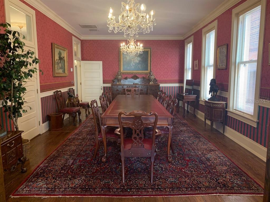 A formal dining room features a long wooden table, ornate chandeliers, and patterned red wallpaper — 250 E PARK AVENUE, LAKE WALES, FL