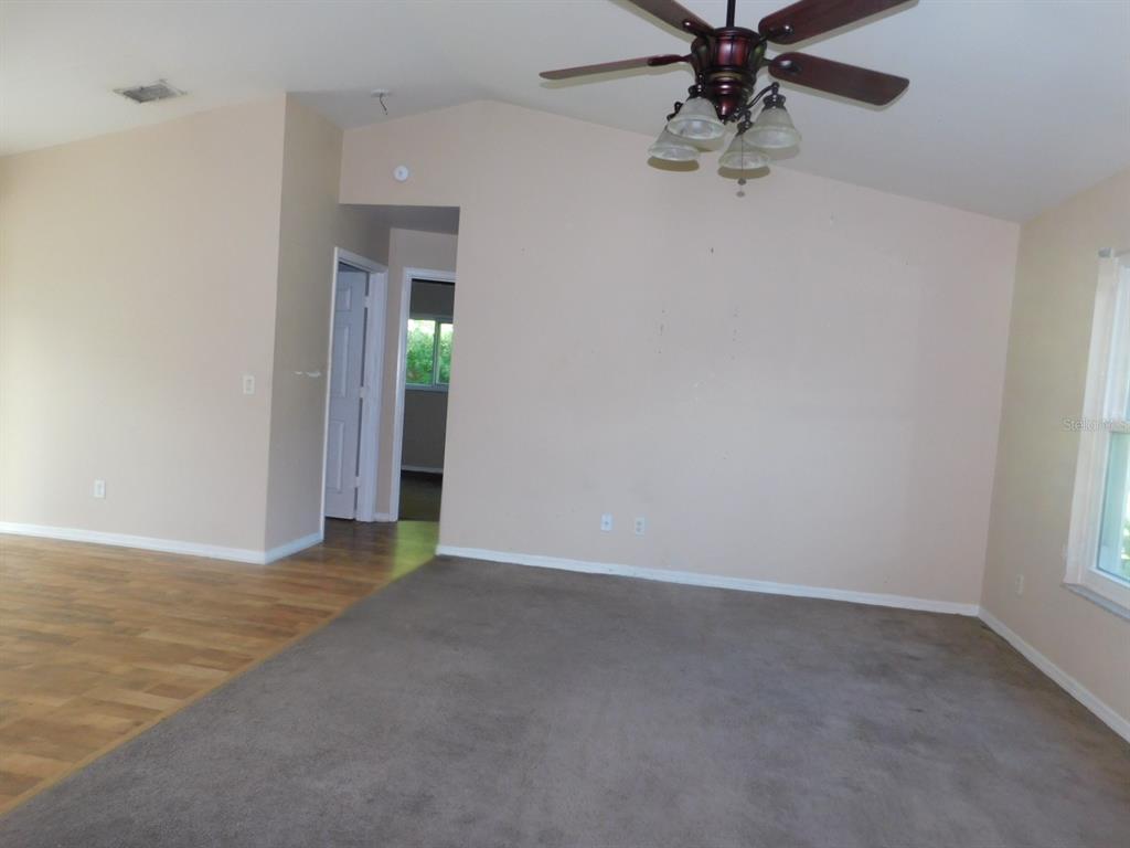 A living room features a vaulted ceiling, a ceiling fan, carpeted flooring, and beige walls — 2637 TISHMAN AVENUE, NORTH PORT, FL