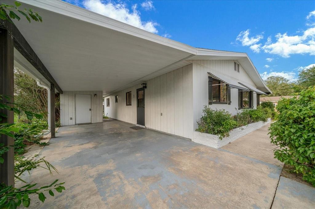 A white house exterior features a covered carport, a concrete driveway, and a small garden bed — 9200 SW 103RD LANE, OCALA, FL