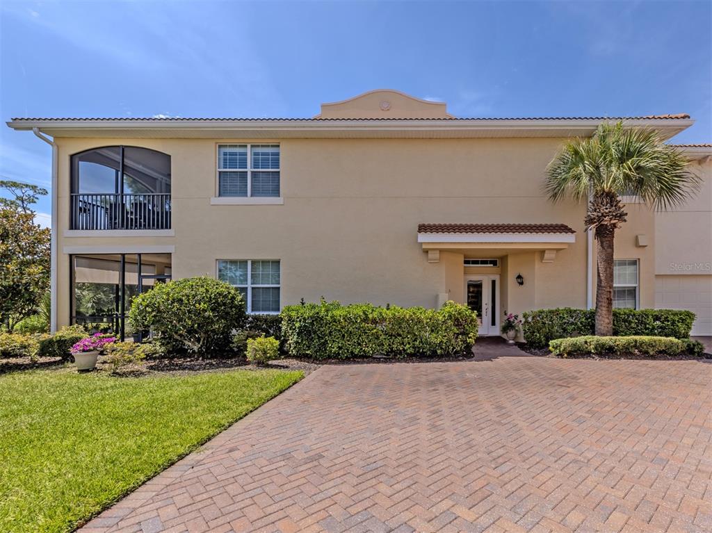 A two-story beige stucco house features a brick driveway, screened balconies, and a palm tree — 194 BELLA VISTA TERRACE UNIT 26A, NORTH VENICE, FL