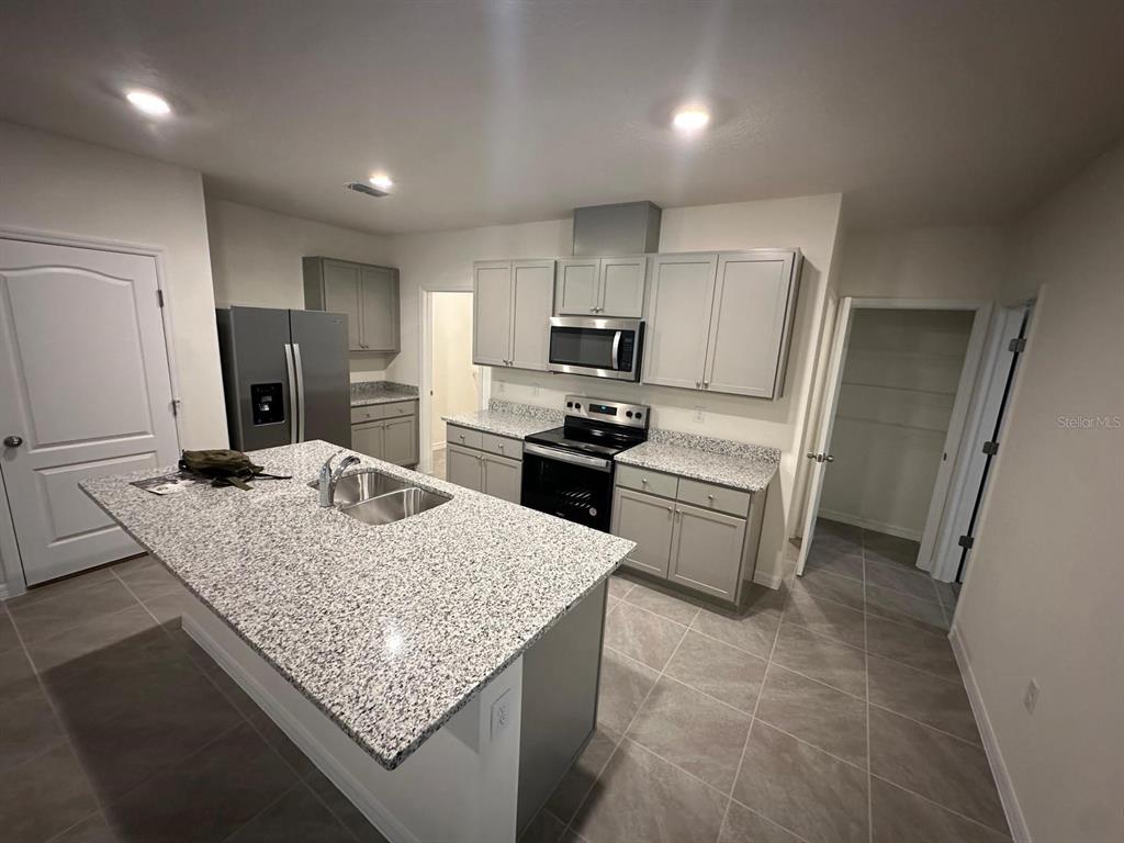 A kitchen features gray cabinets, granite countertops, a center island, and stainless steel appliances — 687 PARK PLACE BOULEVARD, DAVENPORT, FL