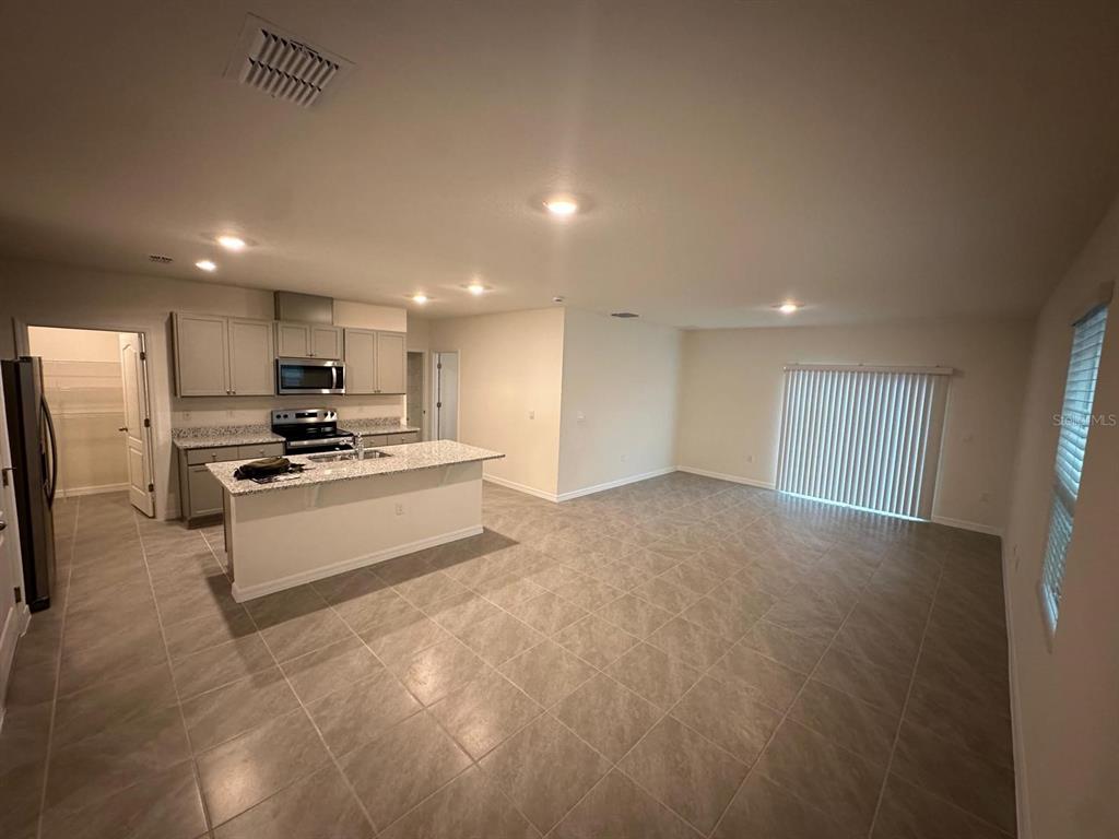 A kitchen with light gray cabinets and a granite island opens to a tiled living area — 687 PARK PLACE BOULEVARD, DAVENPORT, FL
