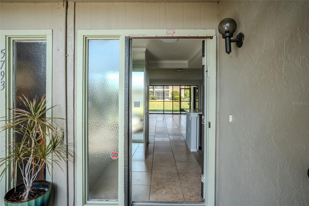 An open front door reveals a tiled interior hallway leading to a screened-in patio area — 5797 SUMMER SIDE LANE UNIT 7A, SARASOTA, FL