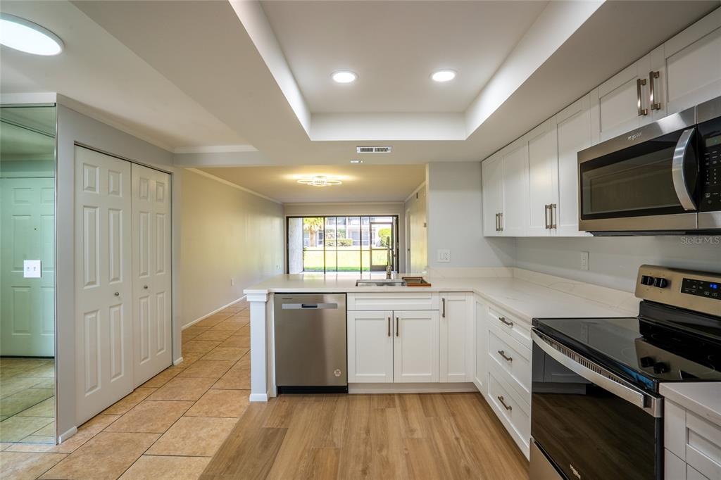 A kitchen with white cabinets, stainless steel appliances, and wood-look flooring opens to a living area — 5797 SUMMER SIDE LANE UNIT 7A, SARASOTA, FL