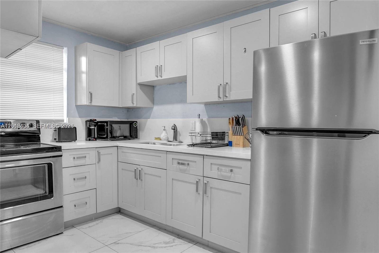 A kitchen features white cabinets, stainless steel appliances, and light-colored tile flooring — 6036 Polk St # 1, Hollywood FL 33024, HOLLYWOOD, FL