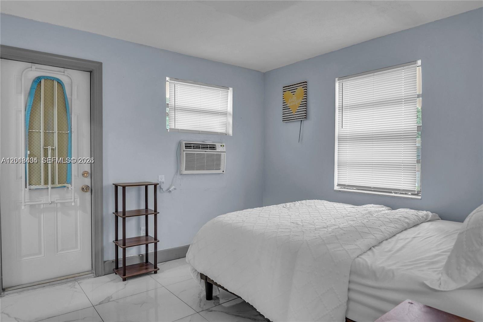 A bedroom features light blue walls, white tile flooring, a bed, and a window unit — 6036 Polk St # 1, Hollywood FL 33024, HOLLYWOOD, FL