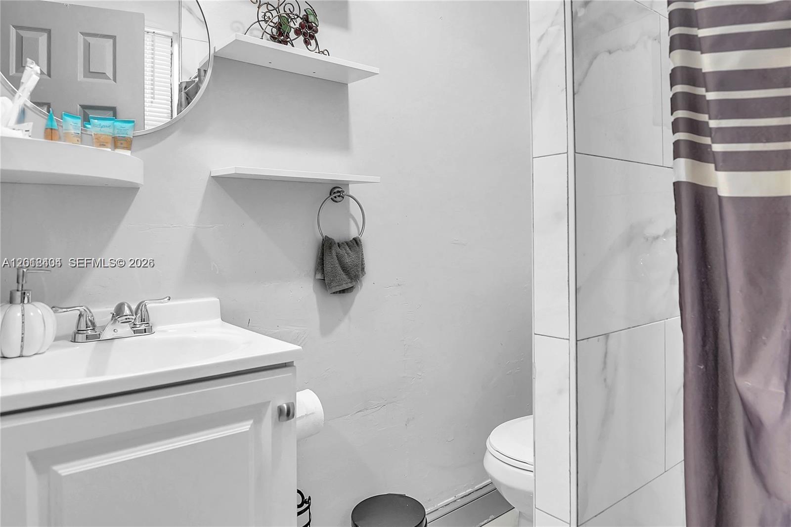 A bathroom features a white vanity, a round mirror, floating shelves, and a tiled shower — 6036 Polk St # 1, Hollywood FL 33024, HOLLYWOOD, FL
