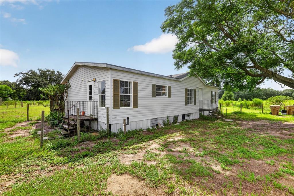 A single-story mobile home with white siding sits on a grassy lot under trees — 25429 SHETLAND TRAIL, SORRENTO, FL
