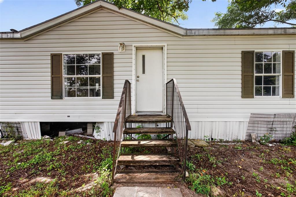 The exterior of a manufactured home features light siding, brown shutters, and wooden front steps — 25429 SHETLAND TRAIL, SORRENTO, FL