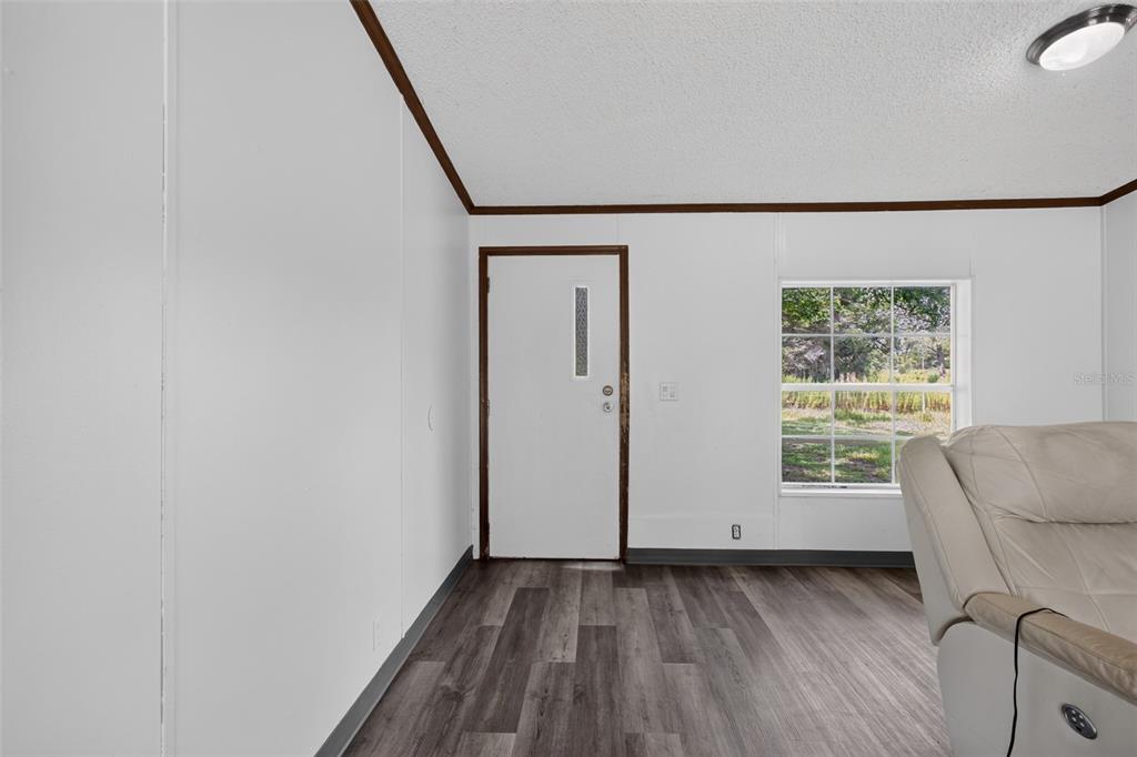A room with white walls, dark wood-look flooring, a white door, and a window — 25429 SHETLAND TRAIL, SORRENTO, FL