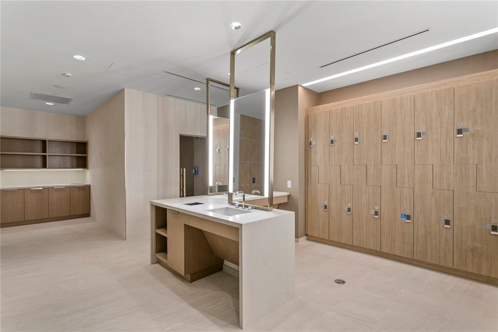 A locker room featuring light wood lockers, a central vanity with a mirror, and tile flooring — 691 S GULFVIEW BOULEVARD UNIT 1011, CLEARWATER BEACH, FL