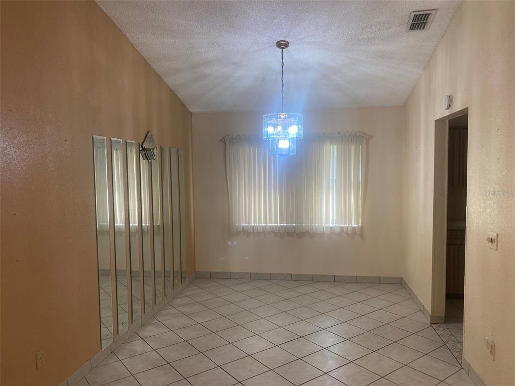 A dining room features tiled floors, a chandelier, vertical wall mirrors, and window blinds — 1101 STILLWATER AVENUE, DELTONA, FL