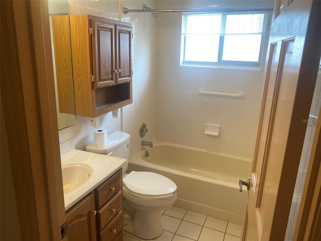 A bathroom features a wooden vanity, a toilet, and a shower-tub combination with white tiles — 1101 STILLWATER AVENUE, DELTONA, FL