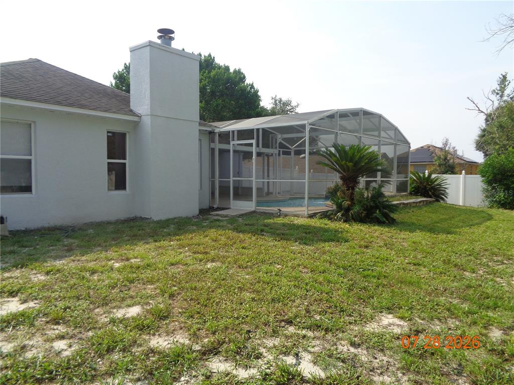 The exterior of a house features a white chimney, a screened-in pool, and a grassy yard — 2610 GROVELAND AVENUE, DELTONA, FL