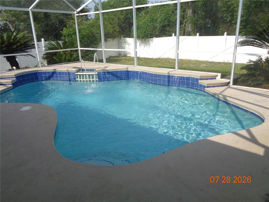 A swimming pool with a fountain and blue tile border sits inside a screened enclosure — 2610 GROVELAND AVENUE, DELTONA, FL