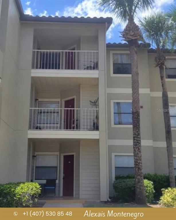 A three-story apartment building exterior features tan siding, white railings, and a tall palm tree — 3008 PARKWAY BOULEVARD UNIT 107, KISSIMMEE, FL