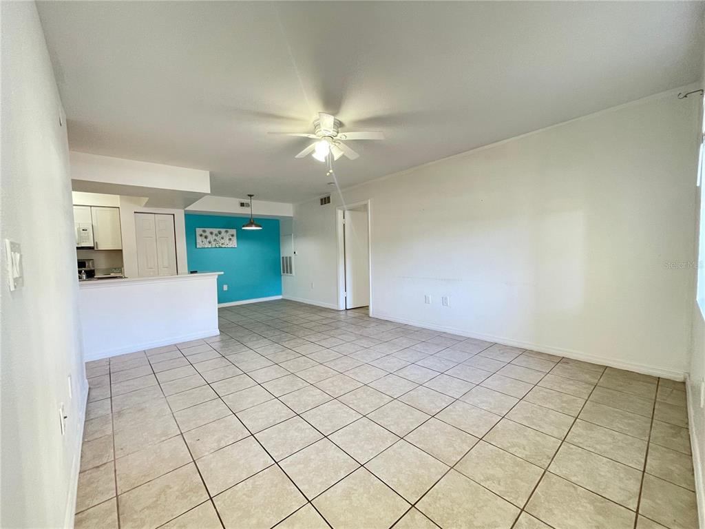 An open-concept living area features light-colored tile flooring, white walls, and a turquoise accent wall — 3008 PARKWAY BOULEVARD UNIT 107, KISSIMMEE, FL