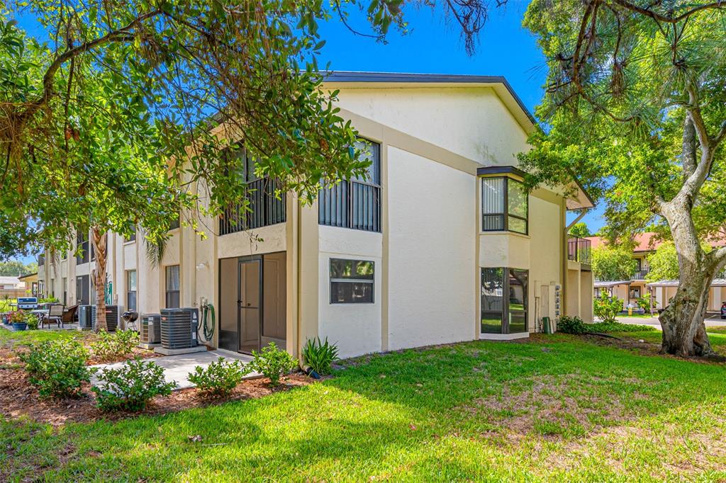 A two-story apartment building exterior with a screened-in patio and surrounding lawn and trees — 11511 113TH STREET UNIT 10A, LARGO, FL