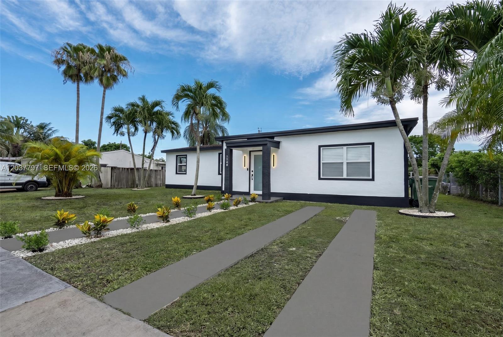 A white single-story house with a black trim, palm trees, and a concrete driveway — 1550 NE 9th Ct, Homestead FL 33033, HOMESTEAD, FL