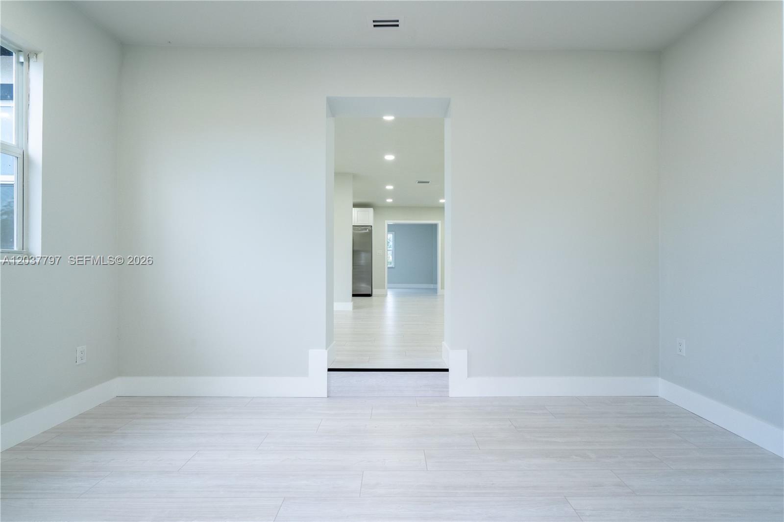 A bright, minimalist room features light-colored wood-look flooring and a doorway leading to another space — 1550 NE 9th Ct, Homestead FL 33033, HOMESTEAD, FL