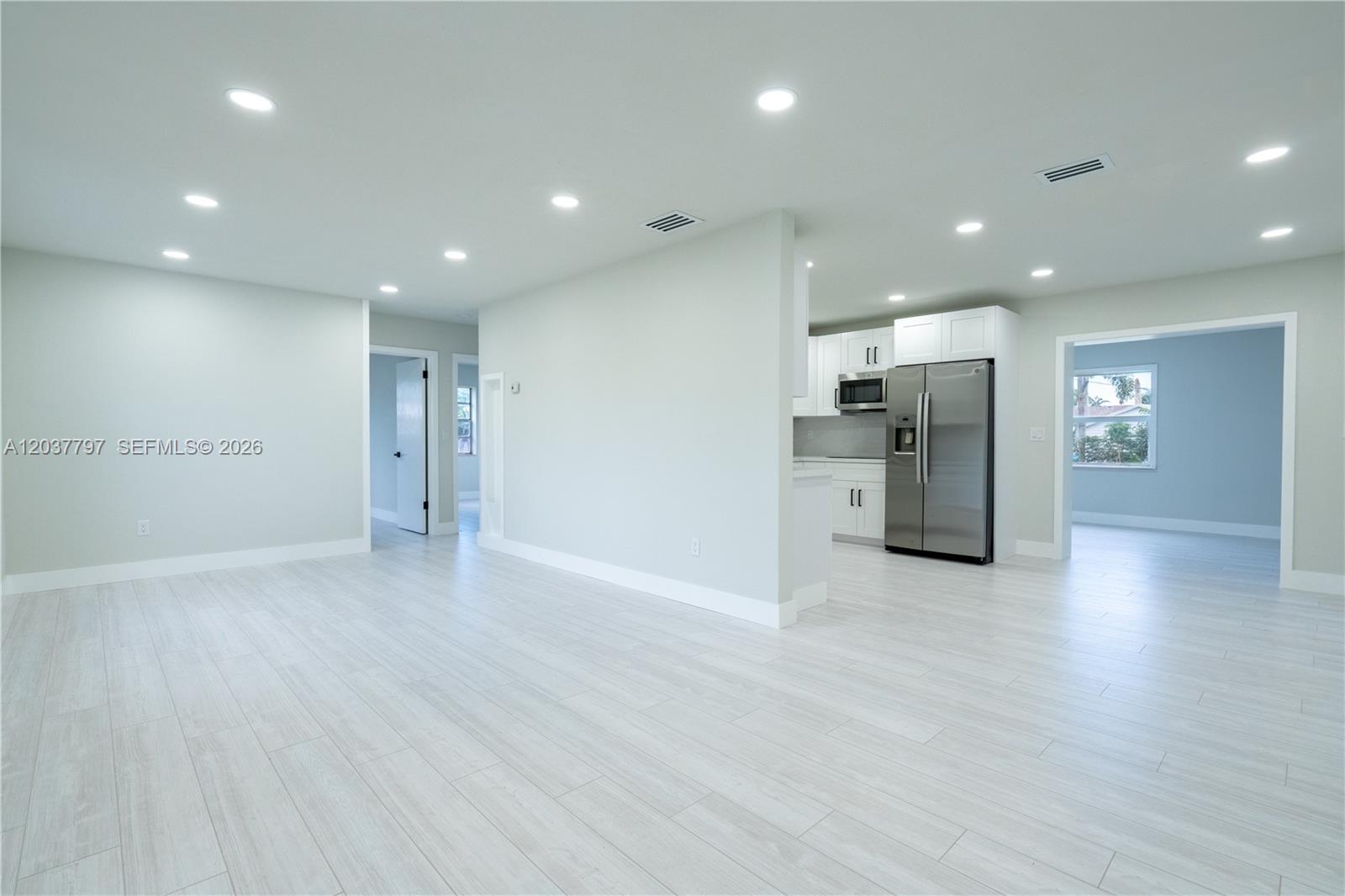 An open-concept living area features light wood-look flooring, recessed lighting, and an adjacent kitchen — 1550 NE 9th Ct, Homestead FL 33033, HOMESTEAD, FL