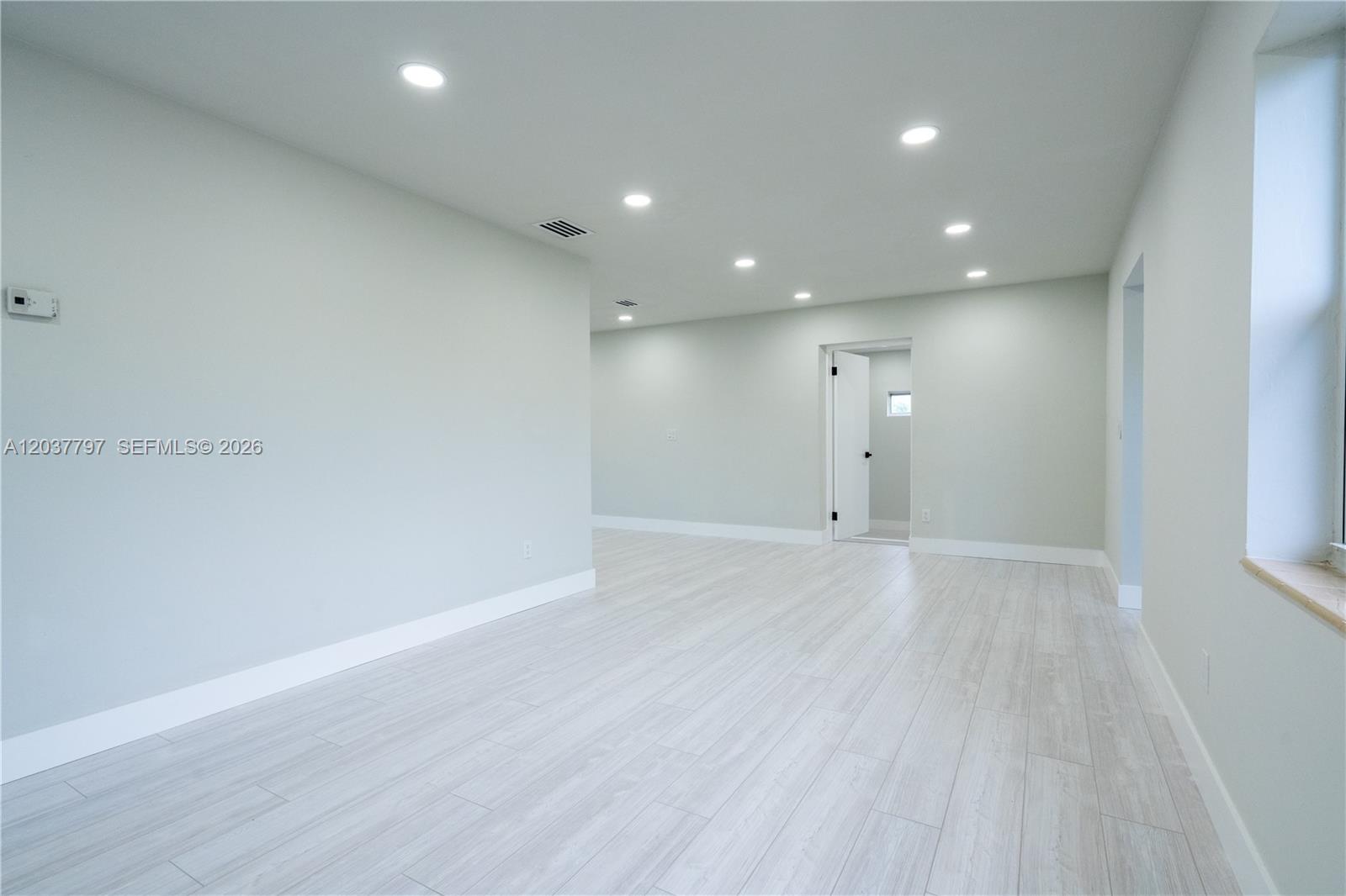 An empty room features light-colored wood-look flooring, recessed ceiling lights, and white walls — 1550 NE 9th Ct, Homestead FL 33033, HOMESTEAD, FL