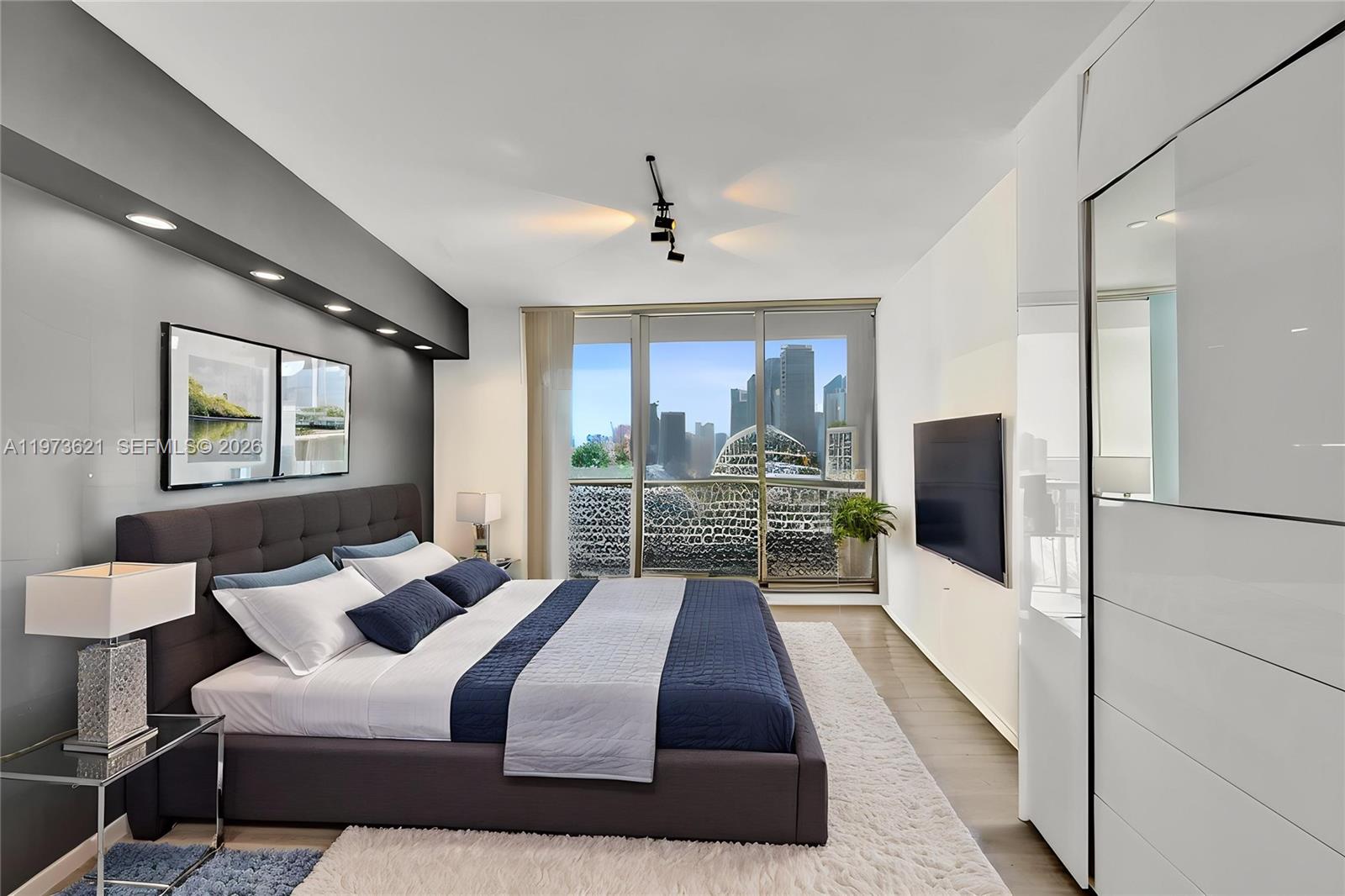A modern bedroom features a dark upholstered bed, recessed lighting, and a city skyline view — 1750 N Bayshore Dr # 2510, Miami FL 33132, MIAMI, FL
