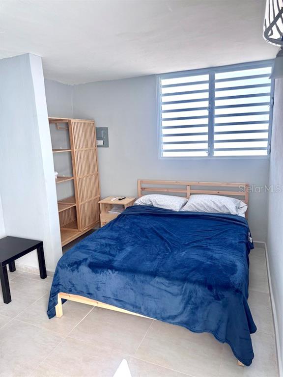 A bedroom features a wooden bed frame with a blue blanket, a wooden shelving unit, and a window — Vistas Del Convento CALLE 3, FAJARDO, PR