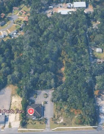 This aerial view shows a commercial building with a parking lot and a large wooded lot — N VOLUSIA AVENUE, ORANGE CITY, FL