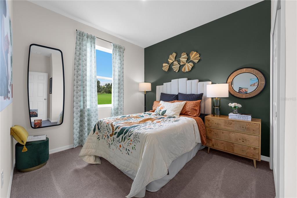 A bedroom features a dark green accent wall, a bed with patterned bedding, and a mirror — 9624 STARLING LOOP, LEESBURG, FL