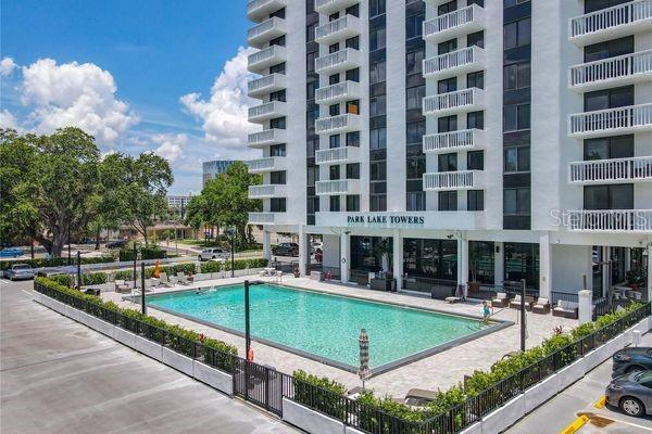 An outdoor swimming pool sits in front of the white Park Lake Towers apartment building — 400 E COLONIAL DRIVE UNIT 1604, ORLANDO, FL