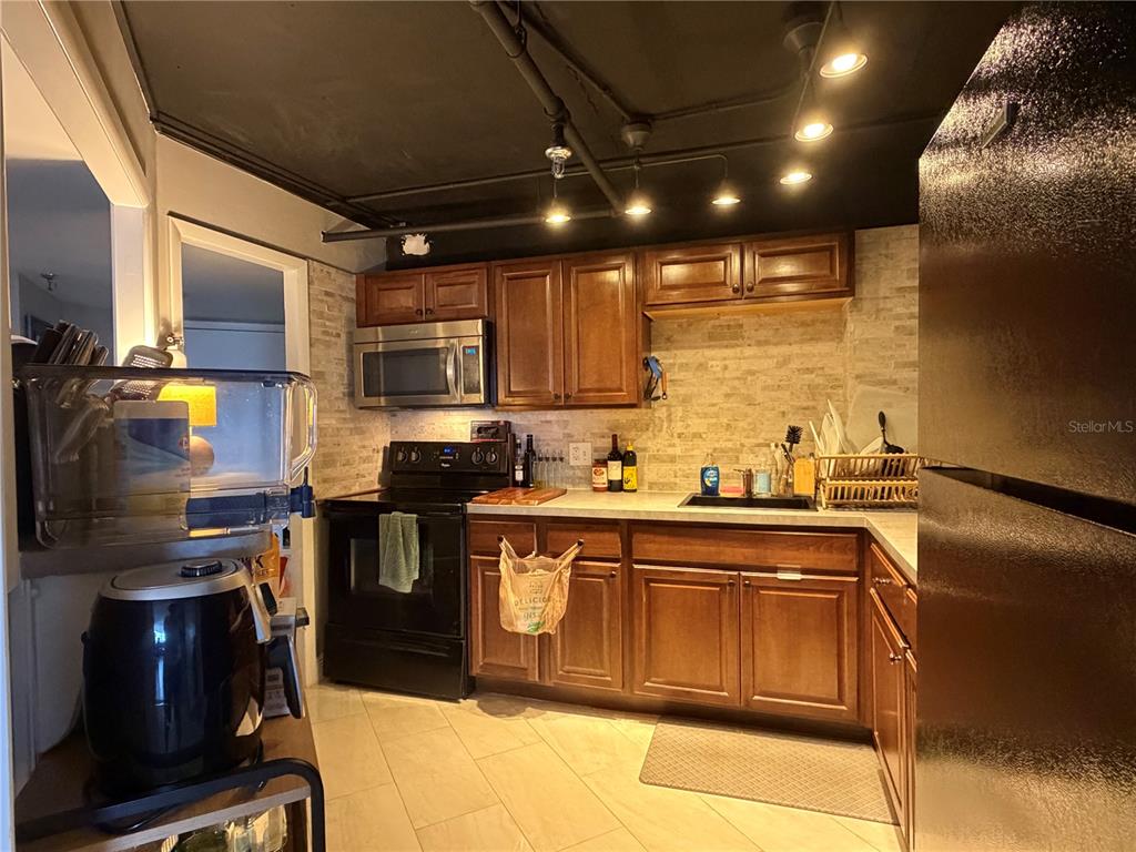 A kitchen features wood cabinets, stainless steel appliances, a brick backsplash, and exposed ceiling lighting — 400 E COLONIAL DRIVE UNIT 1604, ORLANDO, FL