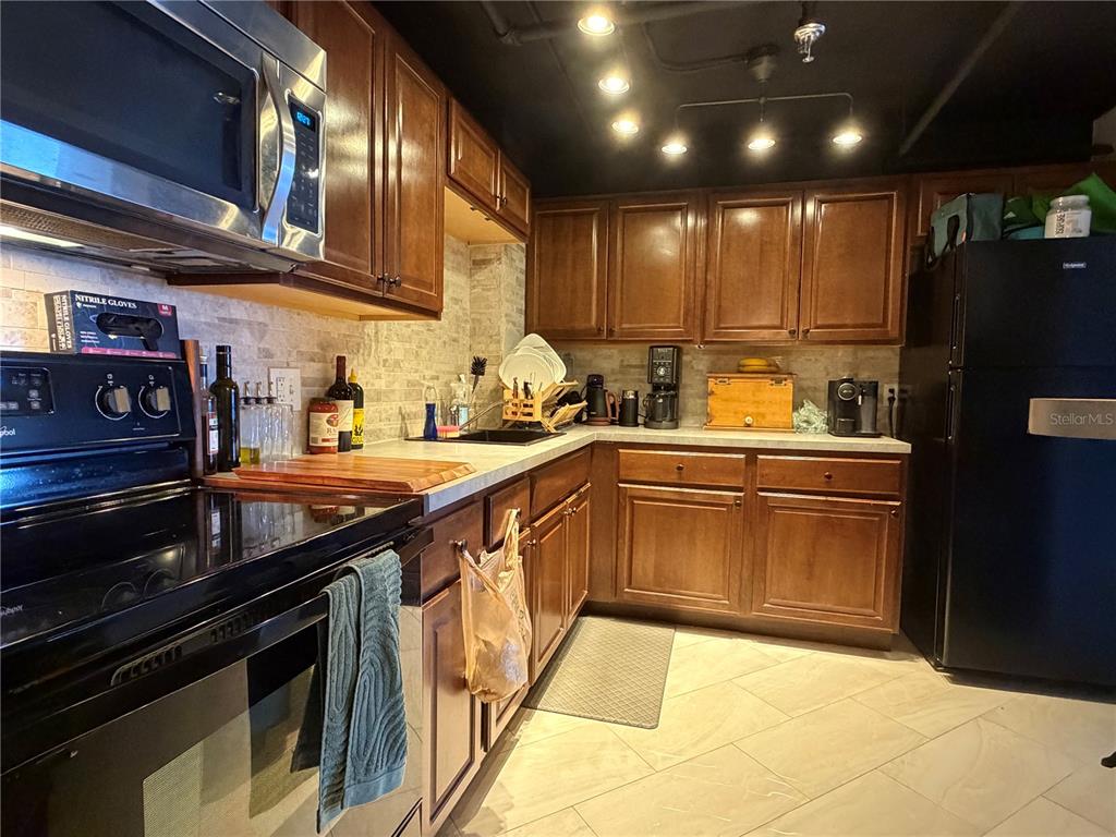 A kitchen features dark wood cabinets, black appliances, a tiled backsplash, and a dark ceiling — 400 E COLONIAL DRIVE UNIT 1604, ORLANDO, FL