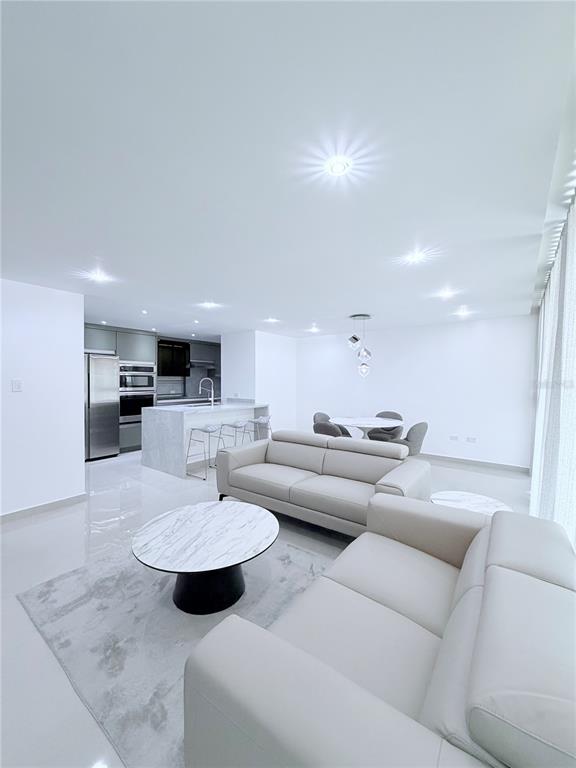 An open-concept living room and kitchen featuring white tile floors, modern furniture, and recessed lighting — PARKSIDE CII UNIT 906, GUAYNABO, PR