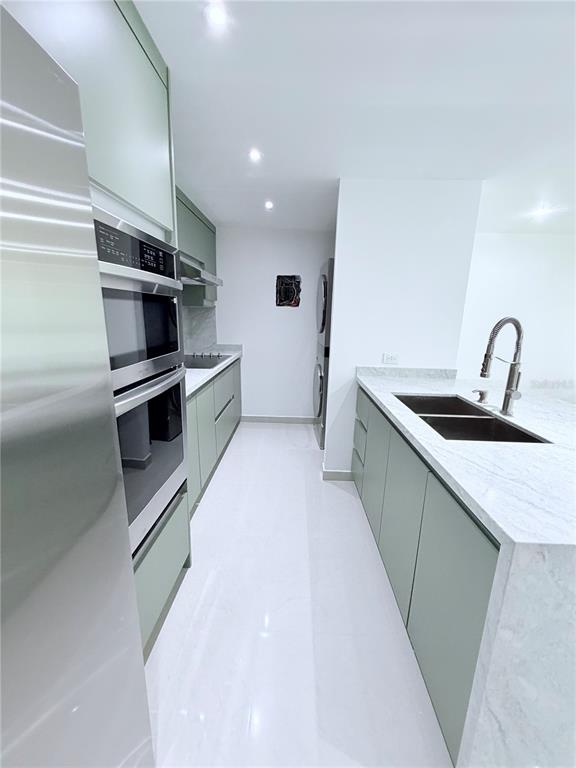 A modern kitchen features sage green cabinetry, white marble countertops, and stainless steel appliances — PARKSIDE CII UNIT 906, GUAYNABO, PR