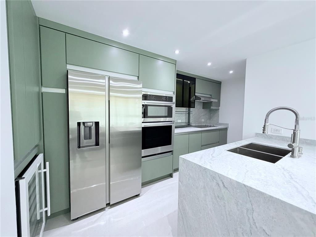 A modern kitchen features sage green cabinetry, stainless steel appliances, and a white marble island — PARKSIDE CII UNIT 906, GUAYNABO, PR