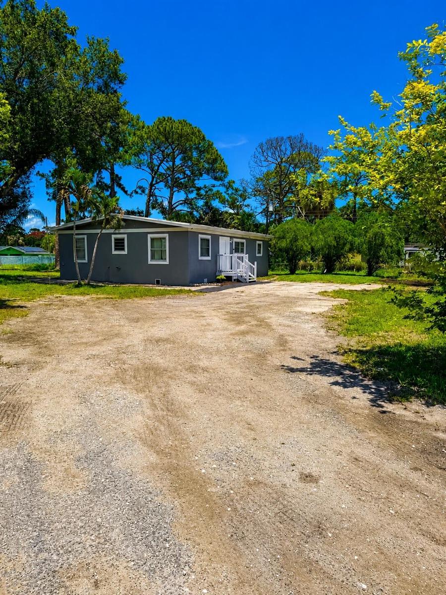 A gray single-story house with a white front porch sits on a large dirt lot — 468 N 53rd Dr Drive N, FL 33415, FL
