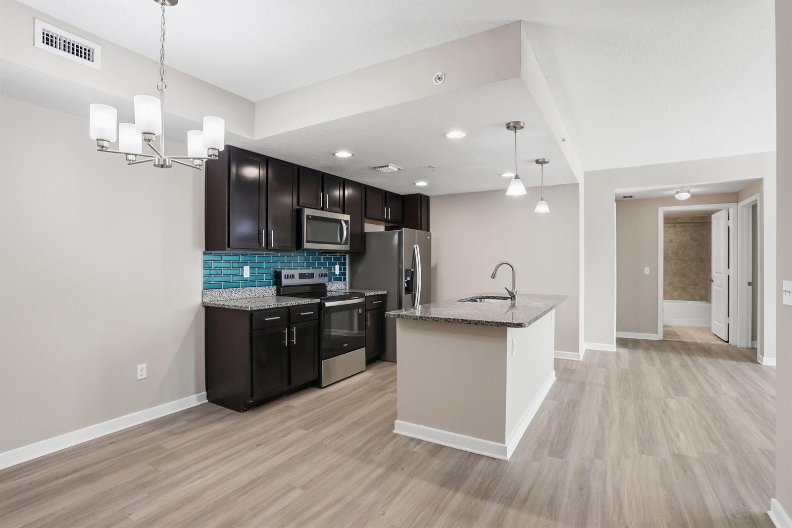 A kitchen features dark wood cabinets, granite countertops, a blue tile backsplash, and an island — 3611 High Ridge Way # 302, Boynton Beach FL 33426, BOYNTON BEACH, FL