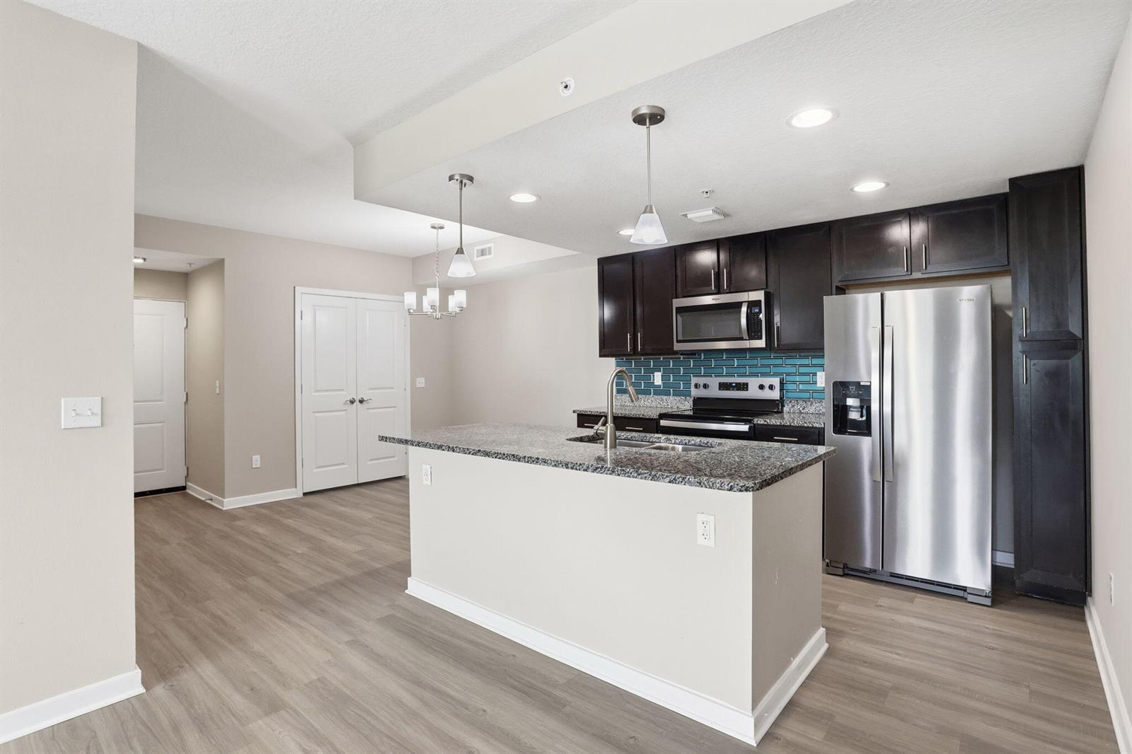 A kitchen features dark wood cabinets, granite countertops, a central island, and stainless steel appliances — 3611 High Ridge Way # 302, Boynton Beach FL 33426, BOYNTON BEACH, FL