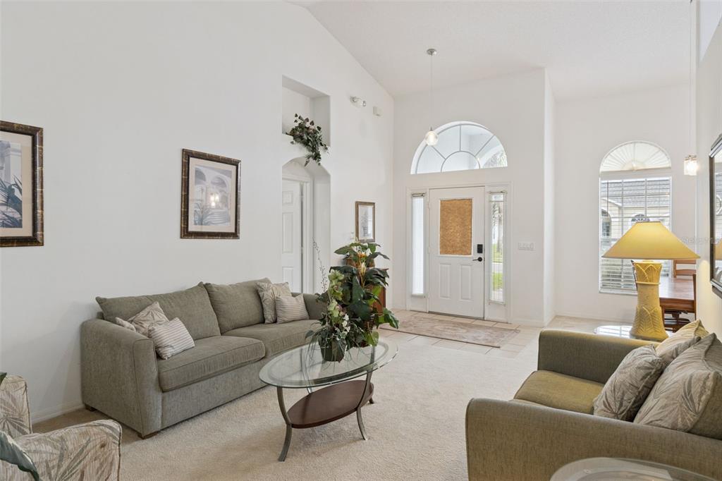 A living room with vaulted ceilings, beige carpet, a glass coffee table, and front entryway — 3144 IBIS HILL STREET, CLERMONT, FL