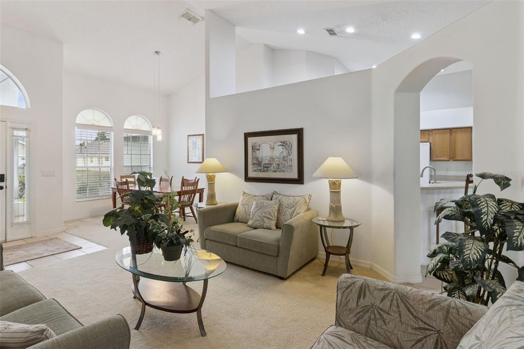 A living room with beige carpet, a loveseat, glass coffee table, and an adjacent dining area — 3144 IBIS HILL STREET, CLERMONT, FL